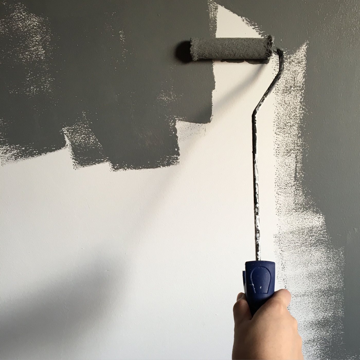 A hand using a paint roller to apply paint to a wall